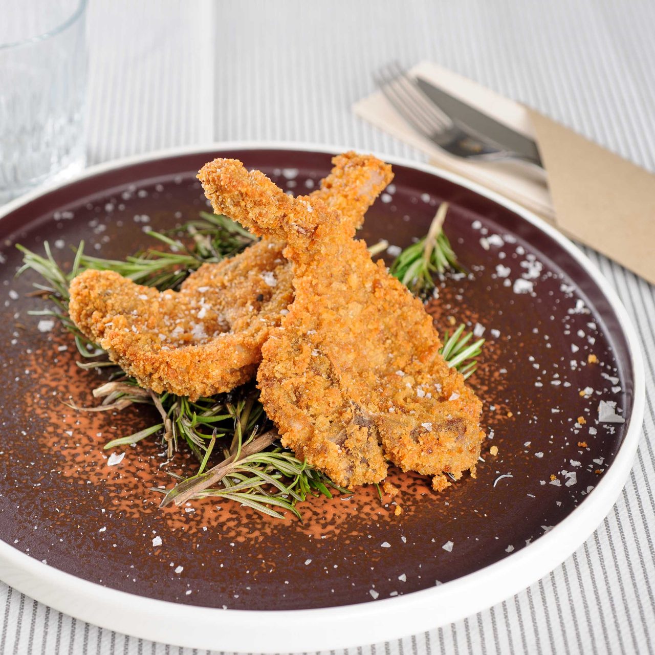 A breaded cutlet plated on a bed of rosemary