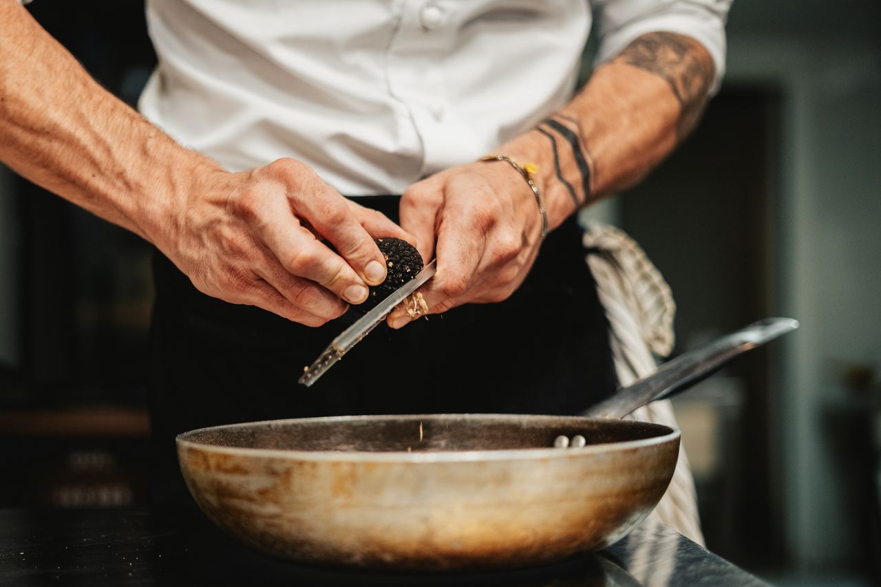 The chef's hands shaving fresh truffle over a copper pan